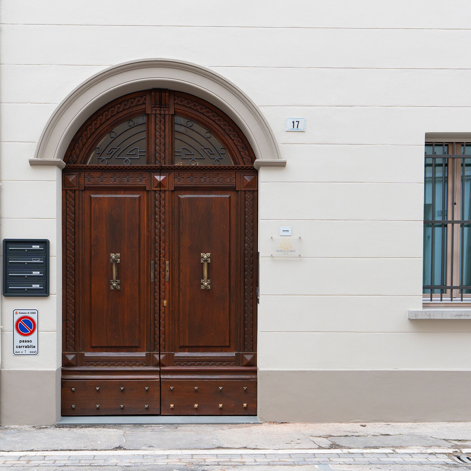 A double wooden door with a decorative arch above it, a mailbox, and a no parking sign on the wall.