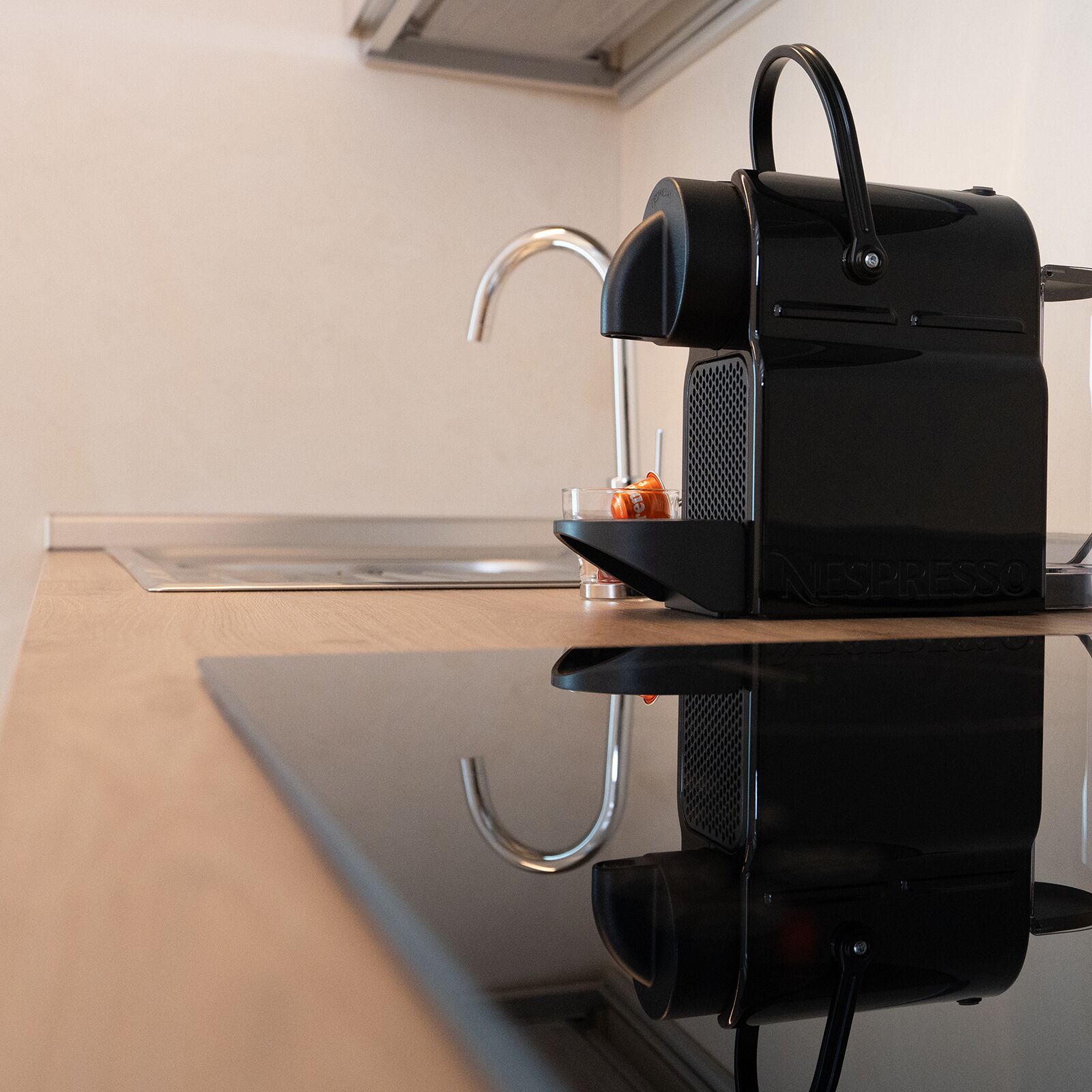 Eine schwarze Espressomaschine auf einer spiegelnden Oberfläche, mit einem kleinen, orangefarbenen Gegenstand darauf.
