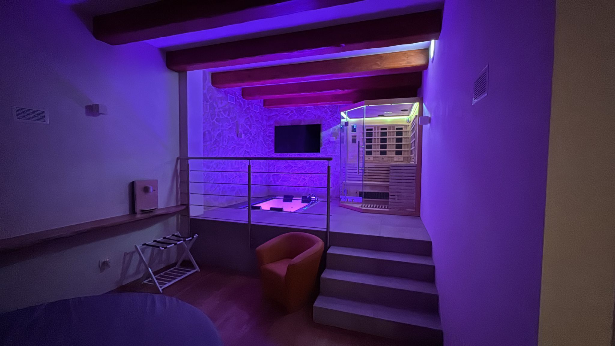 A room with a bed, a chair, a small table, a window, and a staircase.