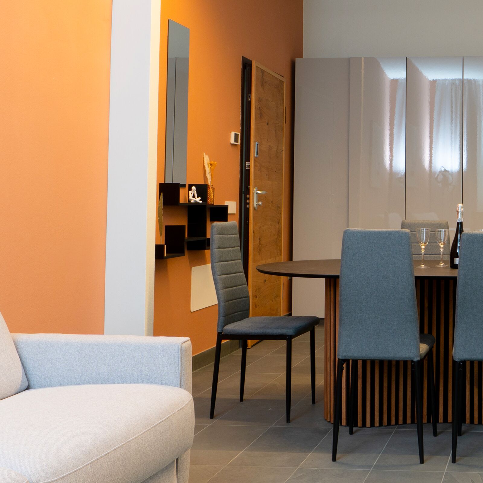 A modern dining area with a wooden table and four chairs, a sofa, and a wooden door.
