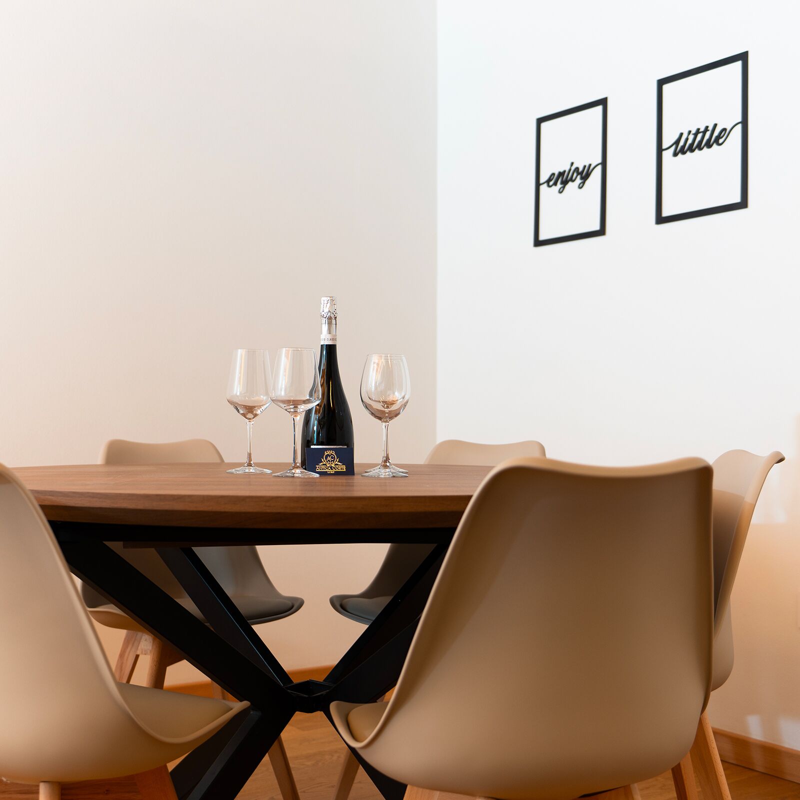 A dining table with a bottle of champagne and three glasses, surrounded by modern chairs.