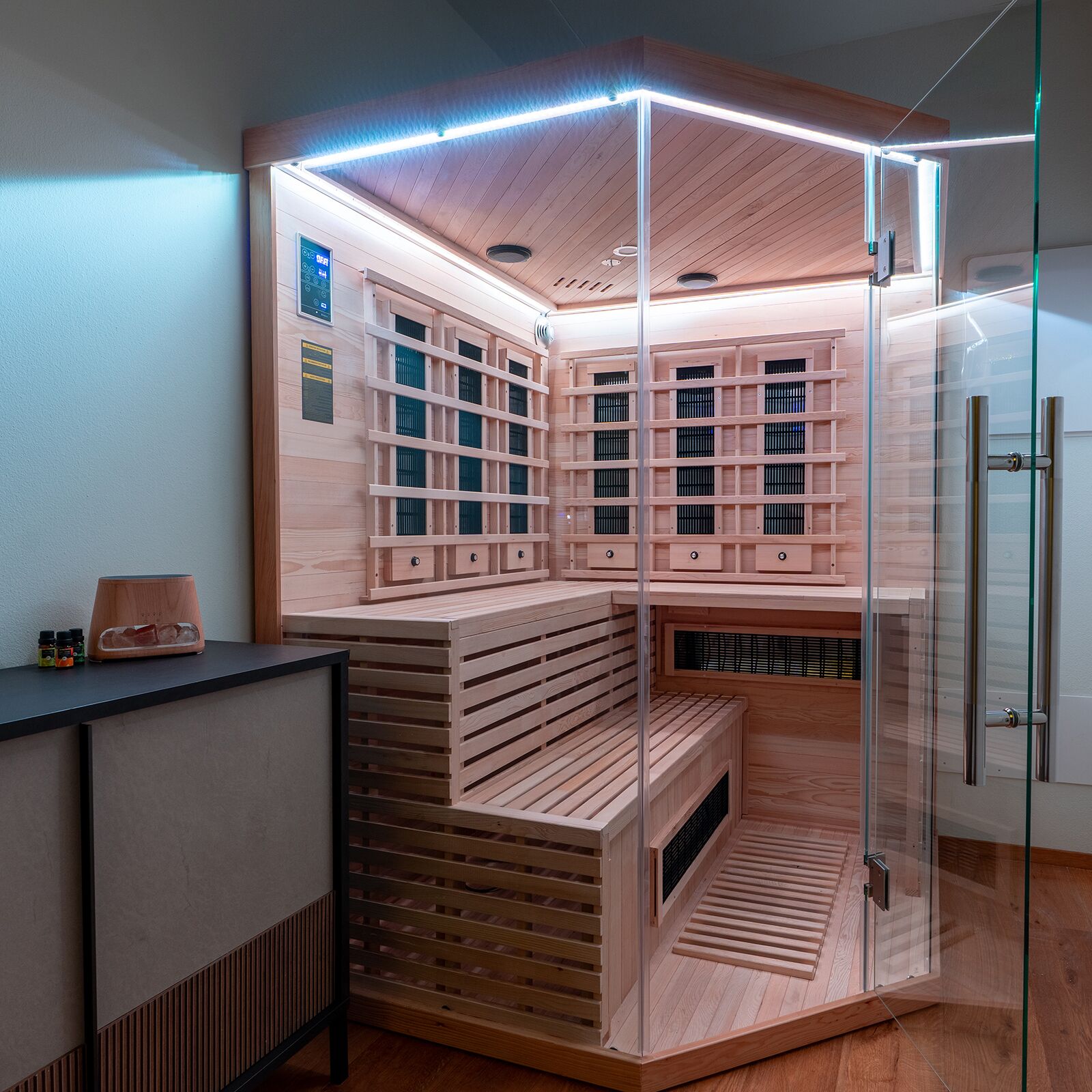 A sauna with multiple benches and a glass enclosure, wooden walls, and a control panel on the left.