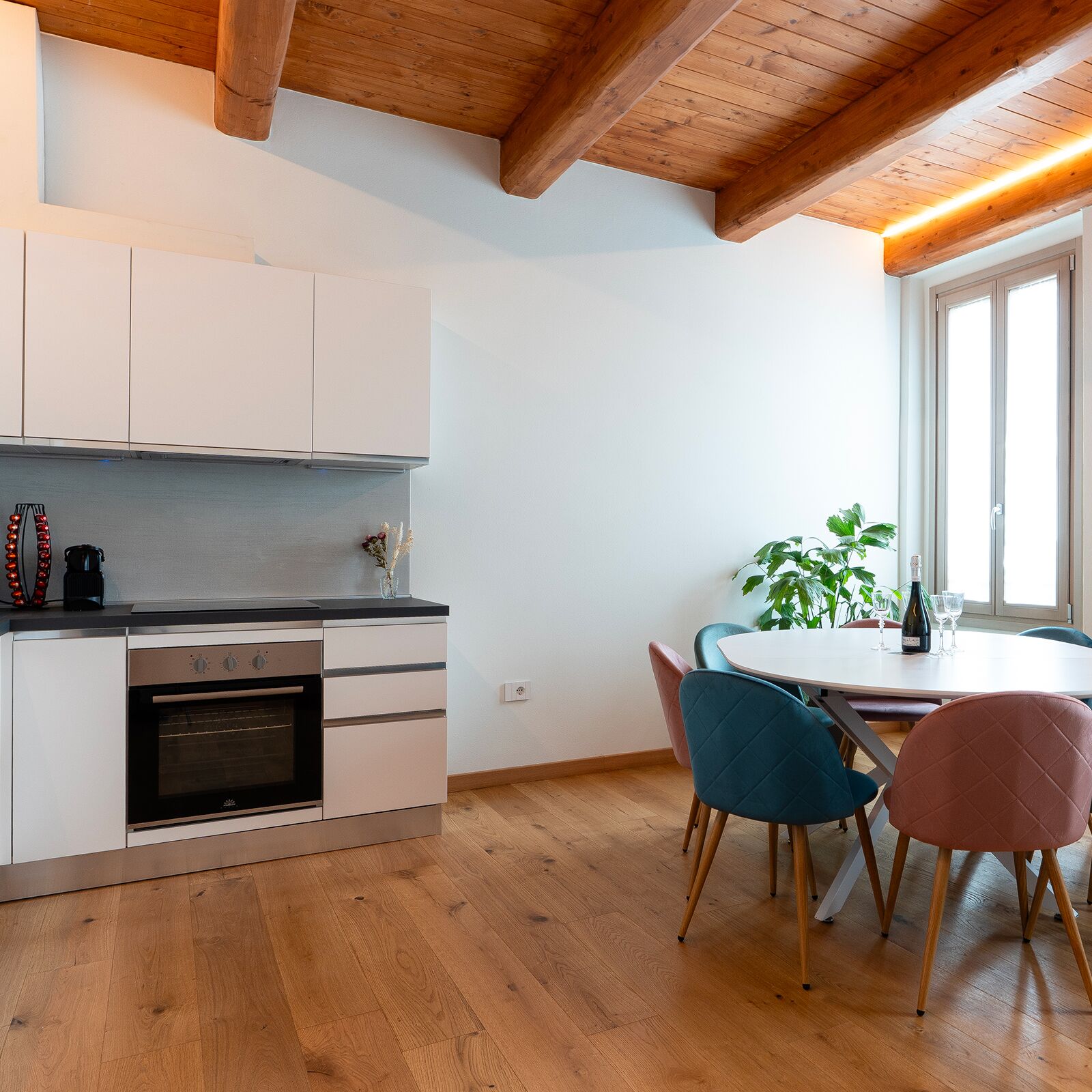A modern kitchen with white cabinets, a built-in oven, and a dining area with a round table and two chairs.
