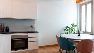 A modern kitchen with white cabinets, a built-in oven, and a dining area with a round table and two chairs.
