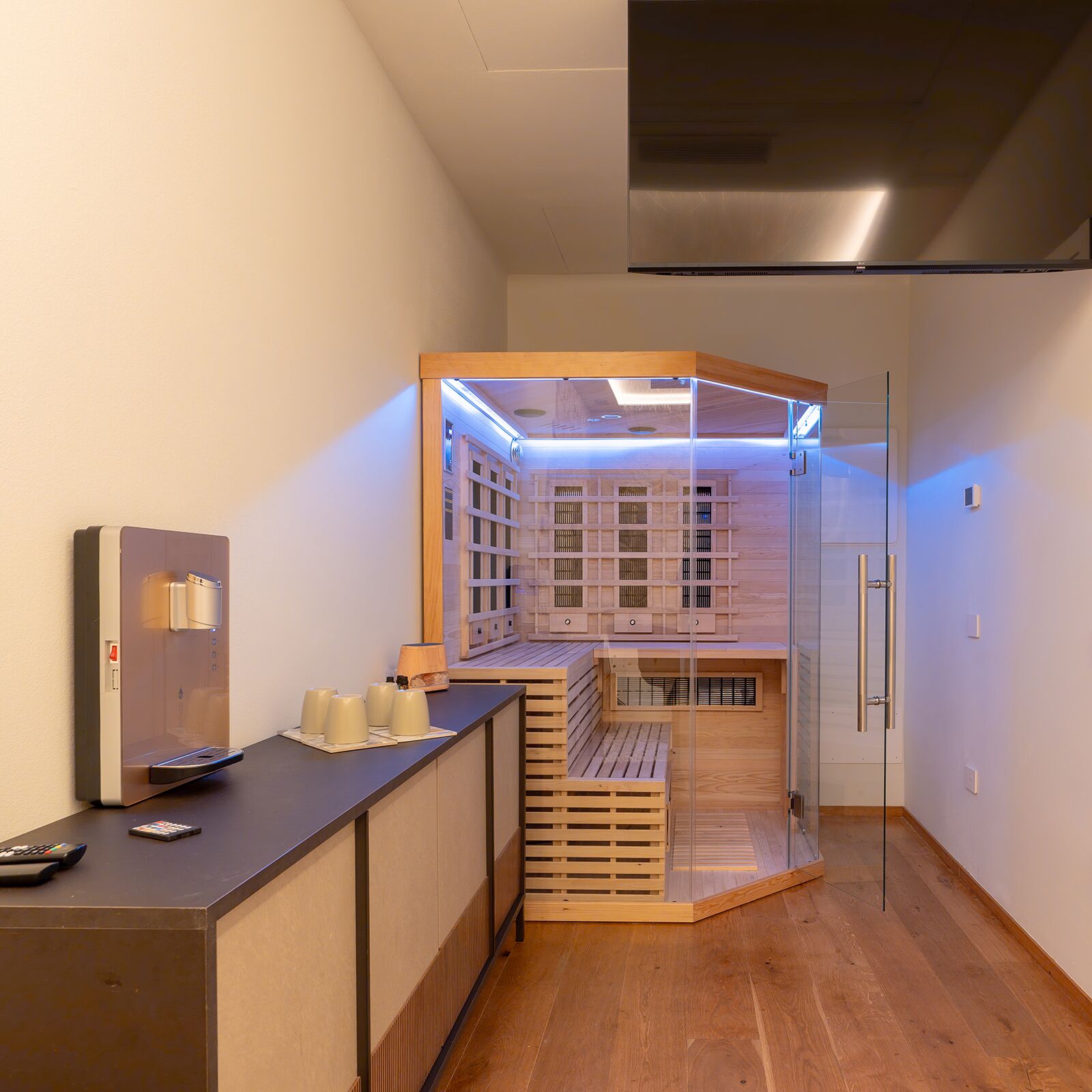 A modern hotel room with a wooden reception desk, a glass partition, and a built-in sauna area.