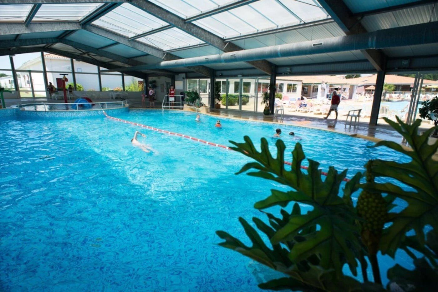 Una piscina techada con carriles delimitados, techo cubierto y servicios visibles junto a la piscina.