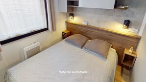 A bedroom with a bed, a window with curtains, a bedside table with a lamp, and a wall-mounted shelf.