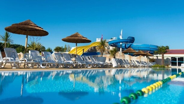 A swimming pool with lounge chairs and umbrellas, a water slide, and a lifeguard tower.