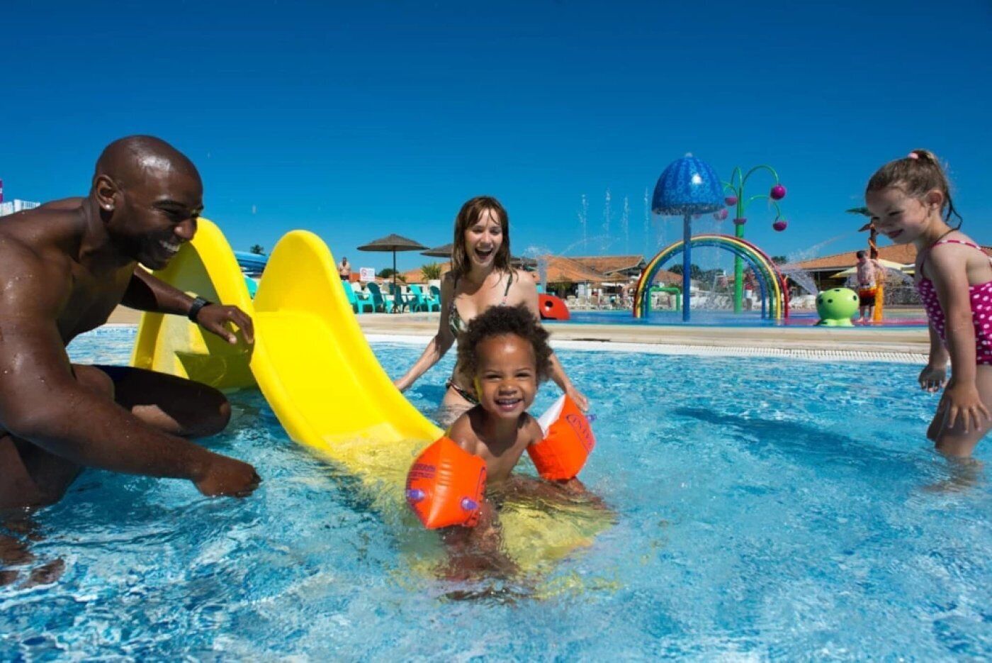 Una piscina con un tobogán amarillo y zona de juegos acuáticos.