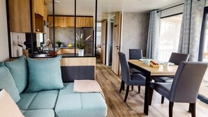 Un salon moderne comprenant un canapé, une table à manger, des chaises et un coin cuisine visible à travers une cloison en verre.