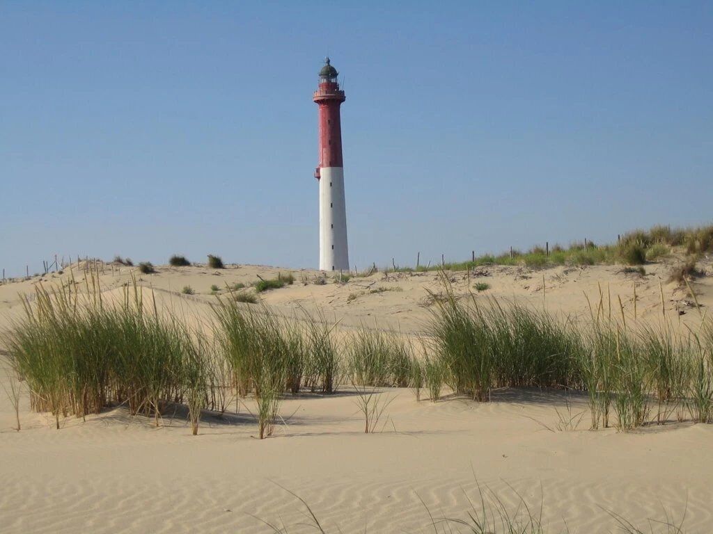 A lighthouse on a sandy beach with sparse vegetation.