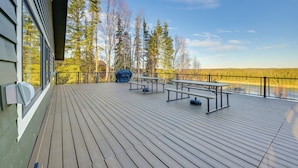 Eine Holzterrasse mit Picknicktischen und einem überdachten Grillbereich mit Blick auf eine bewaldete Landschaft.