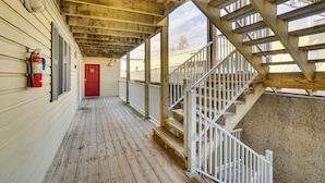 A covered wooden deck with a red door, white railings, and a fire extinguisher mounted on the wall. - Lakefront Osage Beach Condo w/ Water-View Balcony! (Osage Beach)