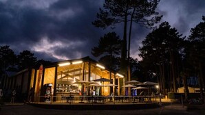 A modern building with a glass facade and an outdoor seating area. - ZEcamping 3* toboggans club enfant locatif clim 28m2 6 pers (Saint-Julien-en-Born)