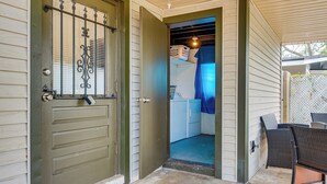 A wooden door with a metal gate, a covered porch with wicker furniture, and a glimpse of a kitchen area with a blue curtain. - 2 Mi to Cocoa Riverfront Park: Home w/ Patio! (Cocoa)
