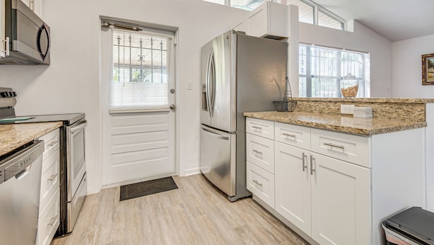 A modern kitchen with white cabinets, stainless steel appliances, and a granite countertop. - 2 Mi to Cocoa Riverfront Park: Home w/ Patio! (Cocoa)
