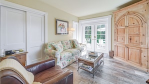 A living room with a brown leather sofa, a floral-patterned couch, a glass coffee table, and a wooden cabinet. - Walk to Beach! Old Naples Escape w/ Patio & Grill (Naples)