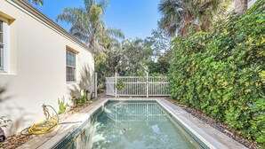 A swimming pool with a white fence, surrounded by lush greenery and a white building. - Walk to Beach! Old Naples Escape w/ Patio & Grill (Naples)