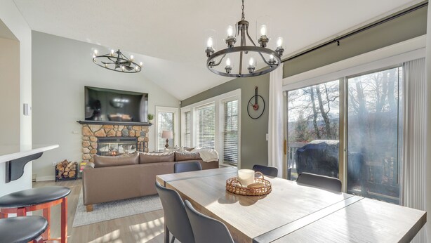 Un vaste espace de vie doté d’une cheminée, d’une table à manger avec des chaises et d’une grande fenêtre avec des stores.