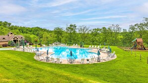 Une piscine entourée d’une pelouse et d’arbres, avec des chaises longues et des parasols à proximité.
