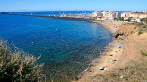 Une plage côtière aux eaux d’un bleu limpide, avec un rivage rocheux et des bâtiments visibles au loin.