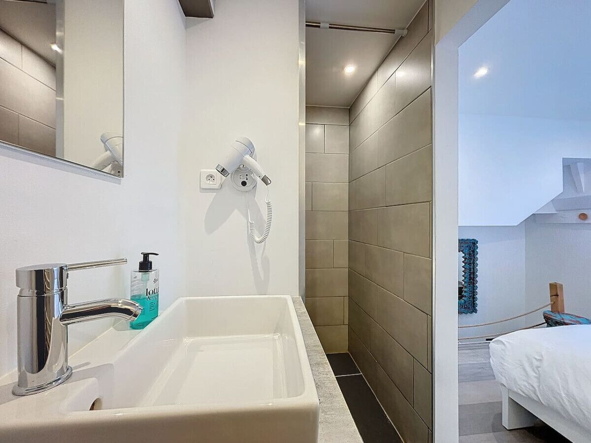 A modern bathroom with a large sink, a mirror, and a hairdryer mounted on the wall.