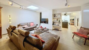 Ett modernt vardagsrum med en lädersoffa, ett soffbord och en tv. I bakgrunden syns en del av köket.