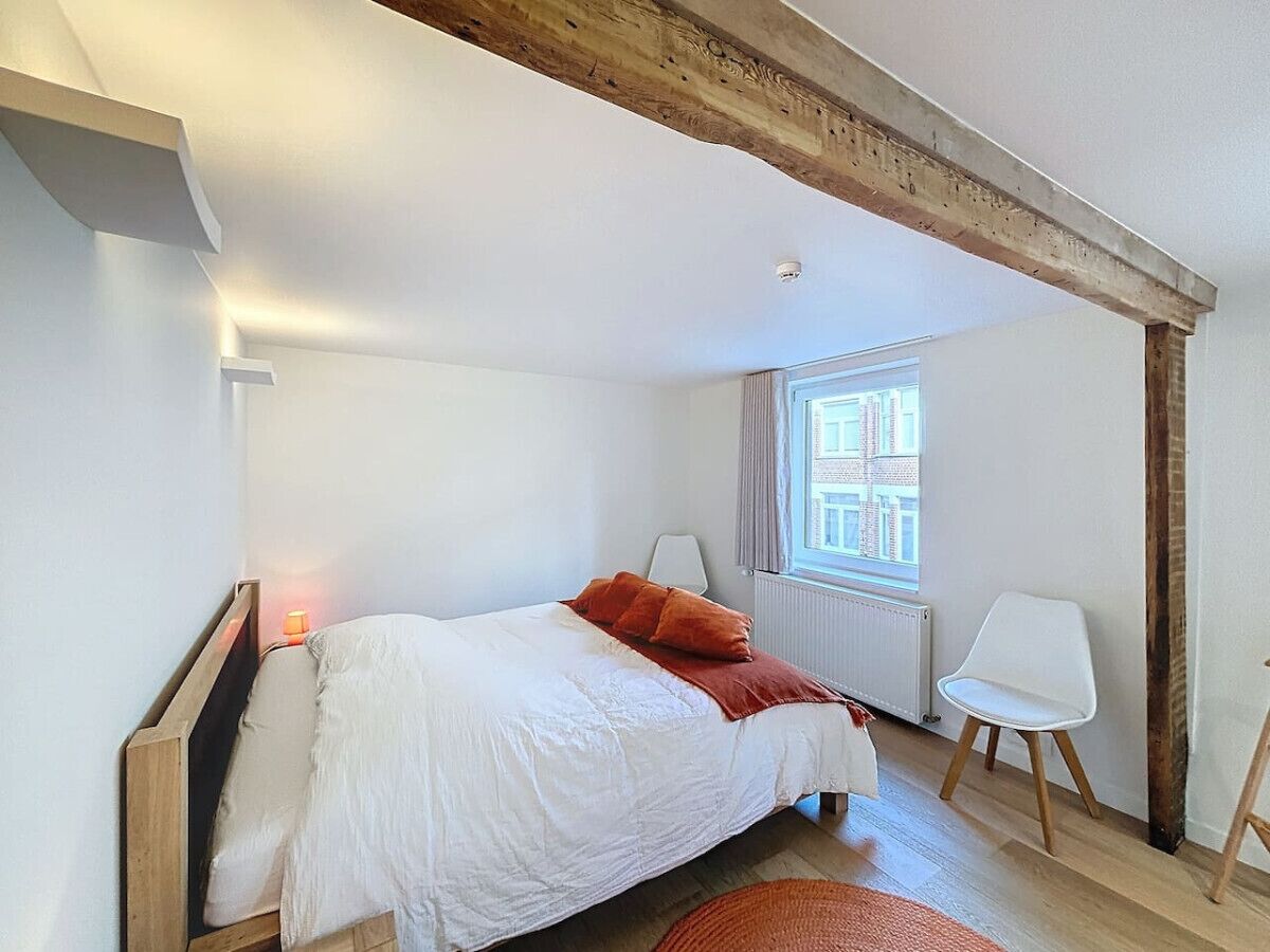 A bedroom with a bed, a chair, a window, and exposed wooden beams.