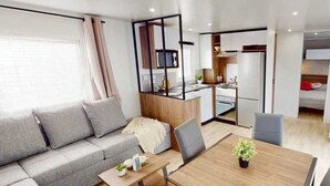 A modern, compact living space with a sofa, a dining table, and a kitchenette. - ZEcamping 4 étoiles familial 1km plage toboggans locatif 36m2 (Les Mathes)