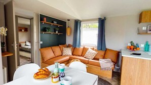 A compact living space with a sofa, a dining table, and a kitchenette. - ZEcamping 4* 1km plage toboggans chiens acceptés locatif clim 36m2 (Les Mathes)