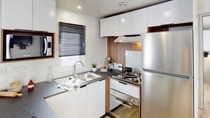 A modern kitchen with white cabinets, stainless steel appliances, a built-in oven, and a window with blinds. - ZEcamping 4 étoiles animé 1km plage toboggans locatif TV LV clim 36m2 (Les Mathes)