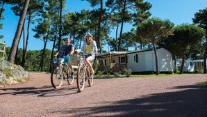 Two people riding bicycles on a gravel path with mobile homes in the background. - ZEcamping 4* animé 1km plage toboggans locatif 36m2 8 pers (Les Mathes)