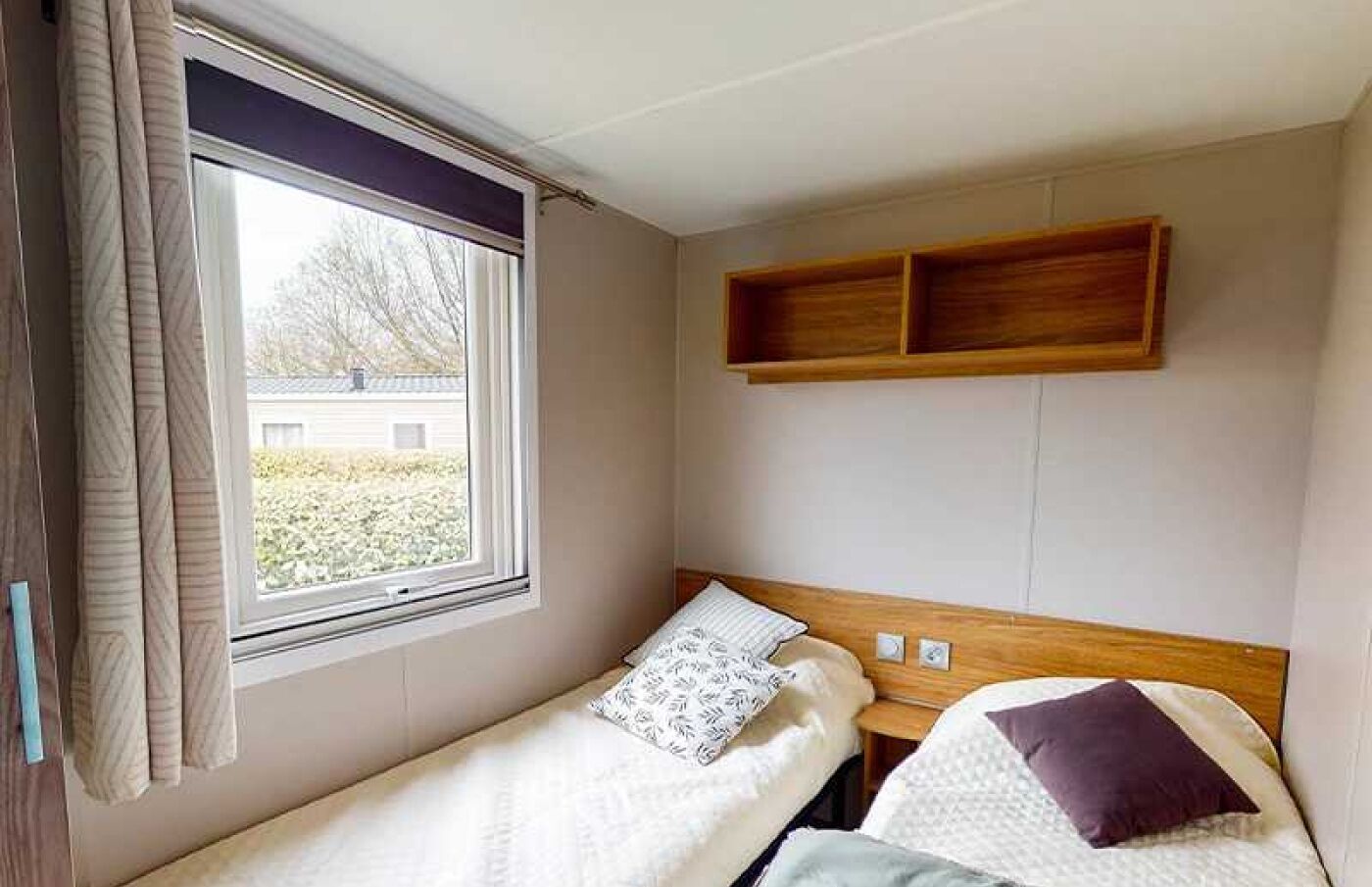 Ein kleines Zimmer mit einem Einzelbett, einem Fenster, einem hölzernen Kopfteil und einem Nachttisch.