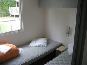 A small, single-bed room with a window, a bedside table, and a built-in bench. - ZEcamping 3 étoiles animaux acceptés bar épicerie et restaurant (Déols)