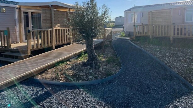 Une rangée de maisons mobiles dotées de terrasses en bois, séparées par un chemin de gravier.