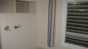 Une chambre à coucher avec un lit, une fenêtre avec des stores, un petit tabouret en bois et un rideau à rayures.