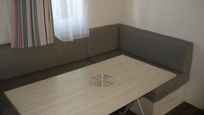 Une pièce d’angle avec un canapé gris, une table en bois surmontée d’un plateau en métal et une fenêtre ornée de rideaux à rayures.