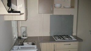 Une cuisine compacte équipée d’une cuisinière à gaz, d’une machine à café et d’un égouttoir à vaisselle.