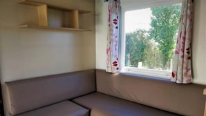 Interior moderno de autocaravana con una zona de asientos tipo banco, una ventana con cortinas florales y un estante de madera encima.