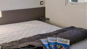 Un dormitorio con cama, ventana, mesita de noche y estante en la pared.