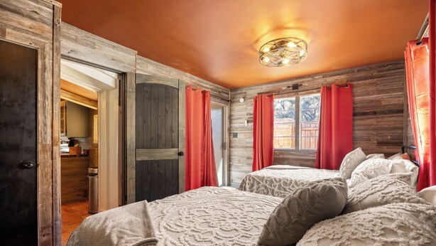 Une chambre avec deux lits, des murs en bois et des rideaux rouges.