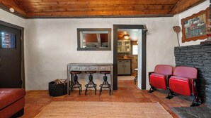 Un salon chaleureux avec une cheminée, un coin repas avec des tabourets et une cuisine visible à travers une porte ouverte.