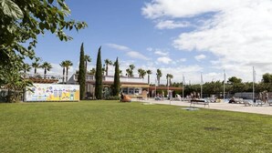 A grassy area with a pool, palm trees, and a building with a mural. - ZEcamping 3 étoiles pataugeoire 200m plage pet friendly locatif TV (Cambrils)