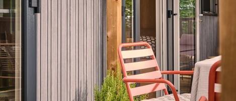 A wooden deck with two chairs, a potted plant, and a sliding glass door leading to an interior space.