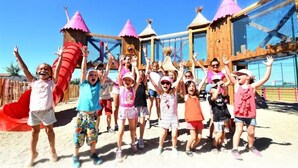 Eine Gruppe Kinder spielt auf einem Spielplatz mit Rutschen und Klettergeräten.