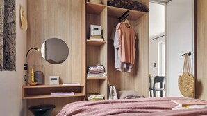 A bedroom with a bed, a wardrobe, a mirror, shelves with books and folded clothes, and a hanging bag. - ZEcamping 4 étoiles animé espace aquatique mobil-home TV LV clim 33m2 (Valras-Plage)
