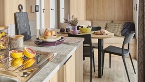 A modern kitchen with a central island, wooden cabinetry, and a dining area with a sofa and chairs. - ZEcamping 4 étoiles animé espace aquatique mobil-home TV LV clim 33m2 (Valras-Plage)