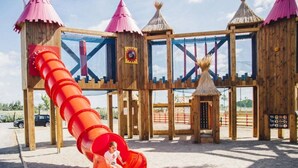 A playground with a red slide and wooden structures. - ZEcamping 4 étoiles animé espace aquatique mobil-home TV LV clim 33m2 (Valras-Plage)