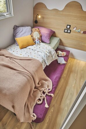A bedroom with a wooden headboard, a bed with a polka dot bedspread, a knitted throw blanket, and a purple cushion.