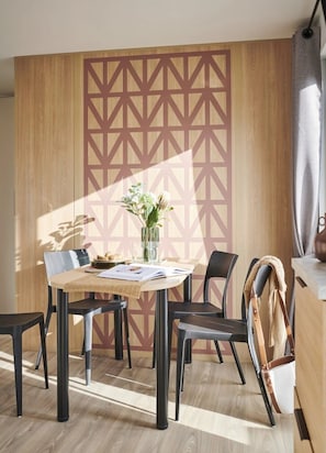 A modern dining area with a geometric patterned wall, a wooden table, and black chairs.